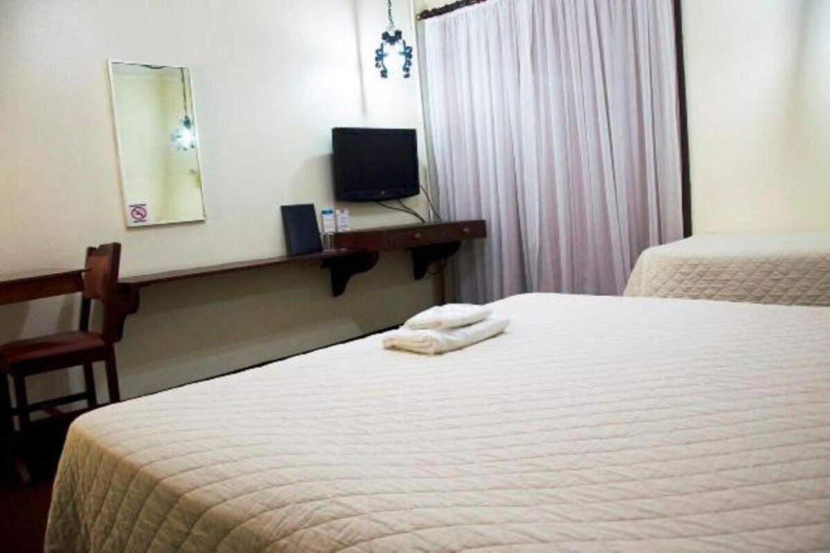 Una habitación de hotel con una cama, una silla, un televisor y una ventana con cortinas.