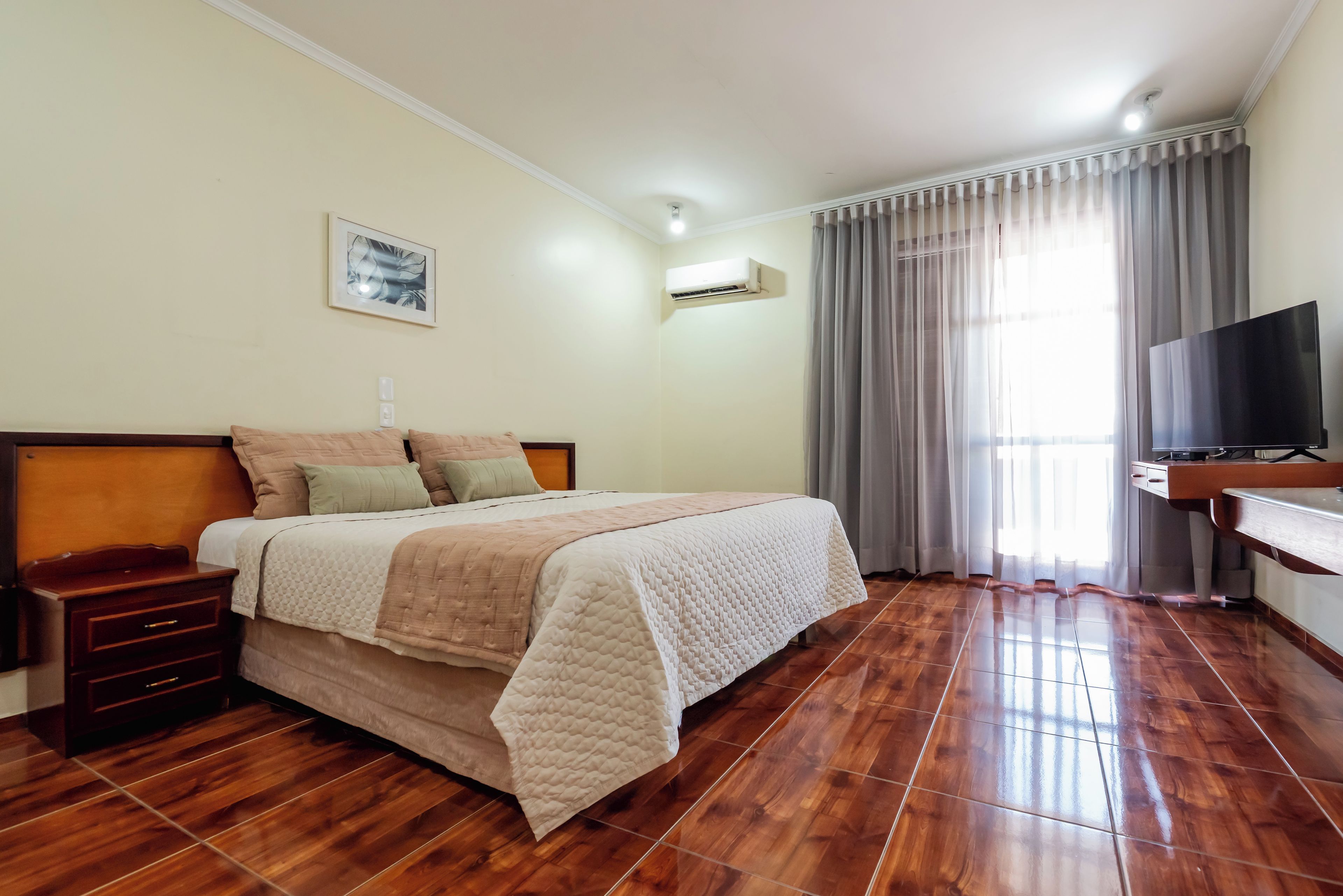 A hotel room with a bed, bedside tables, a TV, and a window with curtains.