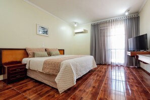 Une chambre d’hôtel avec un lit, des tables de chevet, une télévision et une fenêtre avec des rideaux.