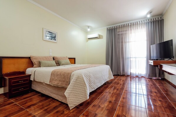 A hotel room with a bed, bedside tables, a TV, and a window with curtains.