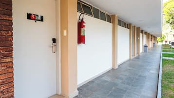 Un pasillo con un extintor fijado en la pared, una puerta con un letrero y una pared de ladrillo en un lateral.