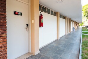 A corridor with a fire extinguisher mounted on the wall, a door with a sign, and a brick wall on one side.