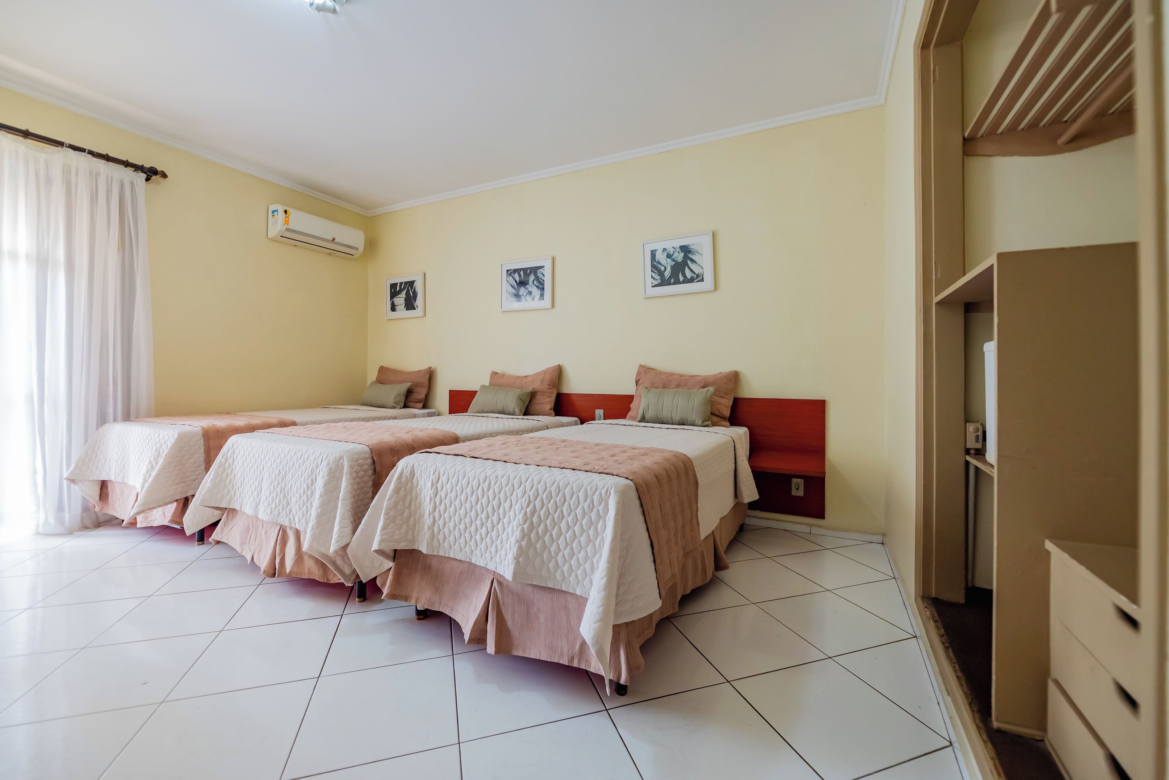 A hotel room with two beds, a wardrobe, and a wall-mounted air conditioner.