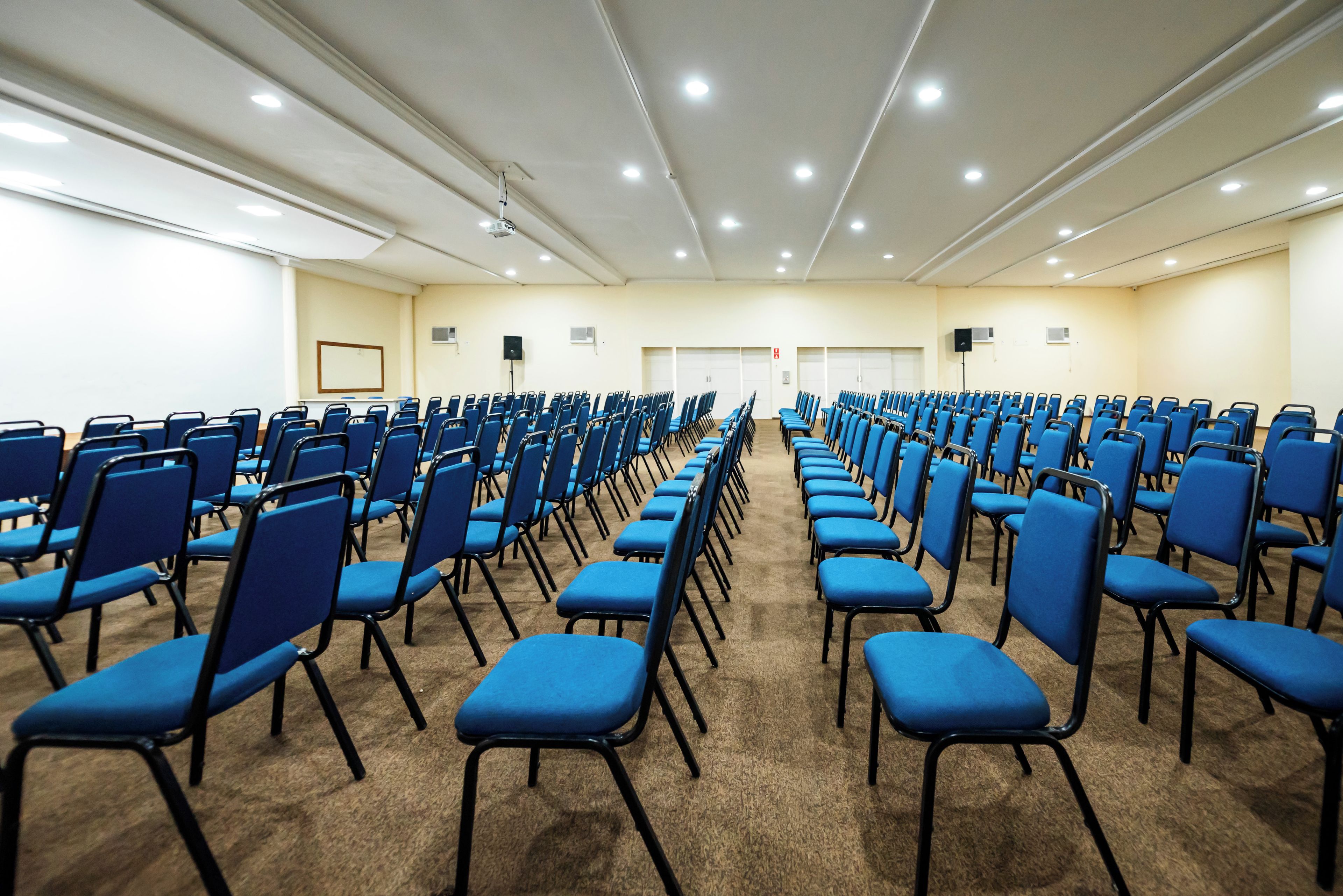 Una sala conferenze con file di sedie blu, una lavagna e un proiettore.