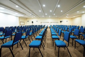 Un salón de conferencias con filas de sillas azules, una pizarra y un proyector.