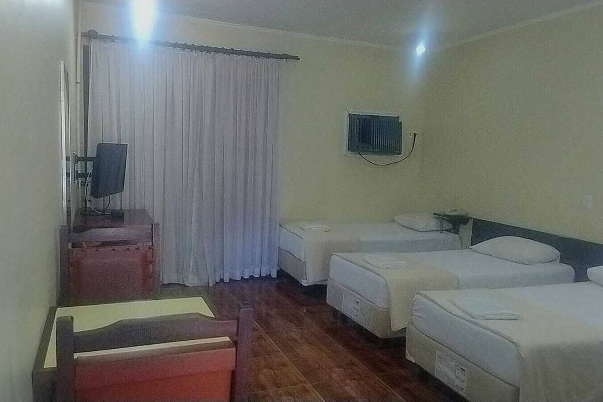 Une chambre d’hôtel avec deux lits simples, un bureau avec une chaise, une petite table et une fenêtre avec des rideaux.