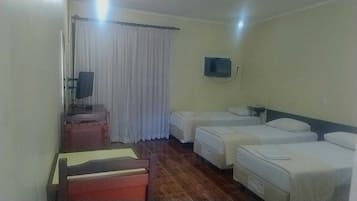 A hotel room with two single beds, a desk with a chair, a small table, and a window with curtains.