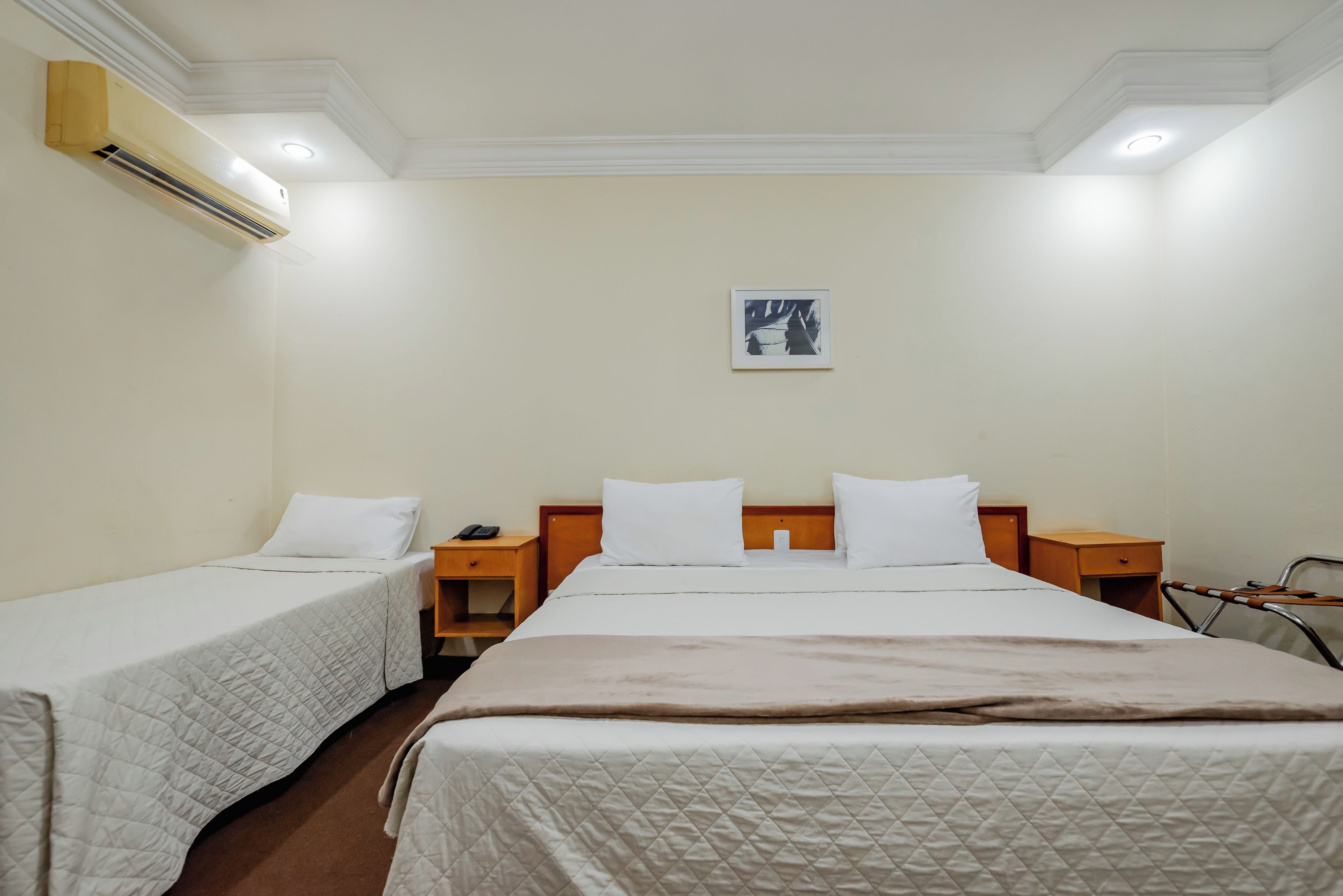 Habitación de hotel con dos camas individuales, una cama grande, una mesita de noche con teléfono y aire acondicionado de pared.