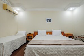 Habitación de hotel con dos camas individuales, una cama grande, una mesita de noche con teléfono y aire acondicionado de pared.