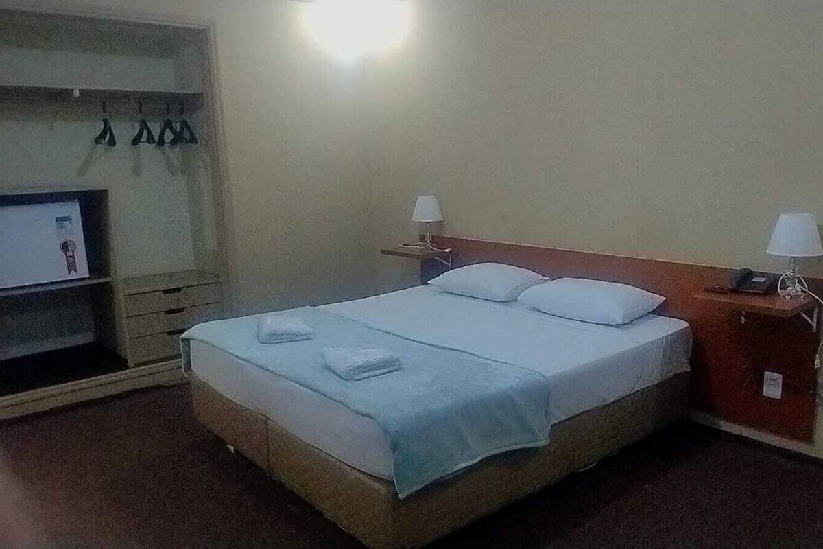Une chambre d’hôtel avec un lit, deux lampes de chevet, un téléviseur posé sur une étagère et une petite table avec un téléphone.