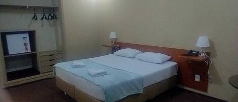 Een hotelkamer met een bed, twee bedlampen, een televisie op een plank en een tafeltje met een telefoon.