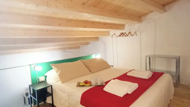 A bedroom with a wooden ceiling, a bed with a red blanket, a bedside table with a lamp, and a small table with a glass top. - Ernesto Home (Palermo)