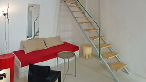 A room with a red sofa, a black chair, a small round table, a mirror, and a wooden staircase. - Ernesto Home (Palermo)