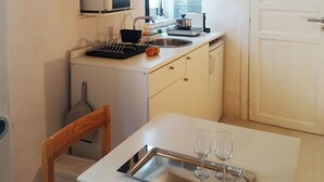 A compact kitchen with a microwave, sink, and a small dining area with a tray table and wine glasses. - Ernesto Home (Palermo)