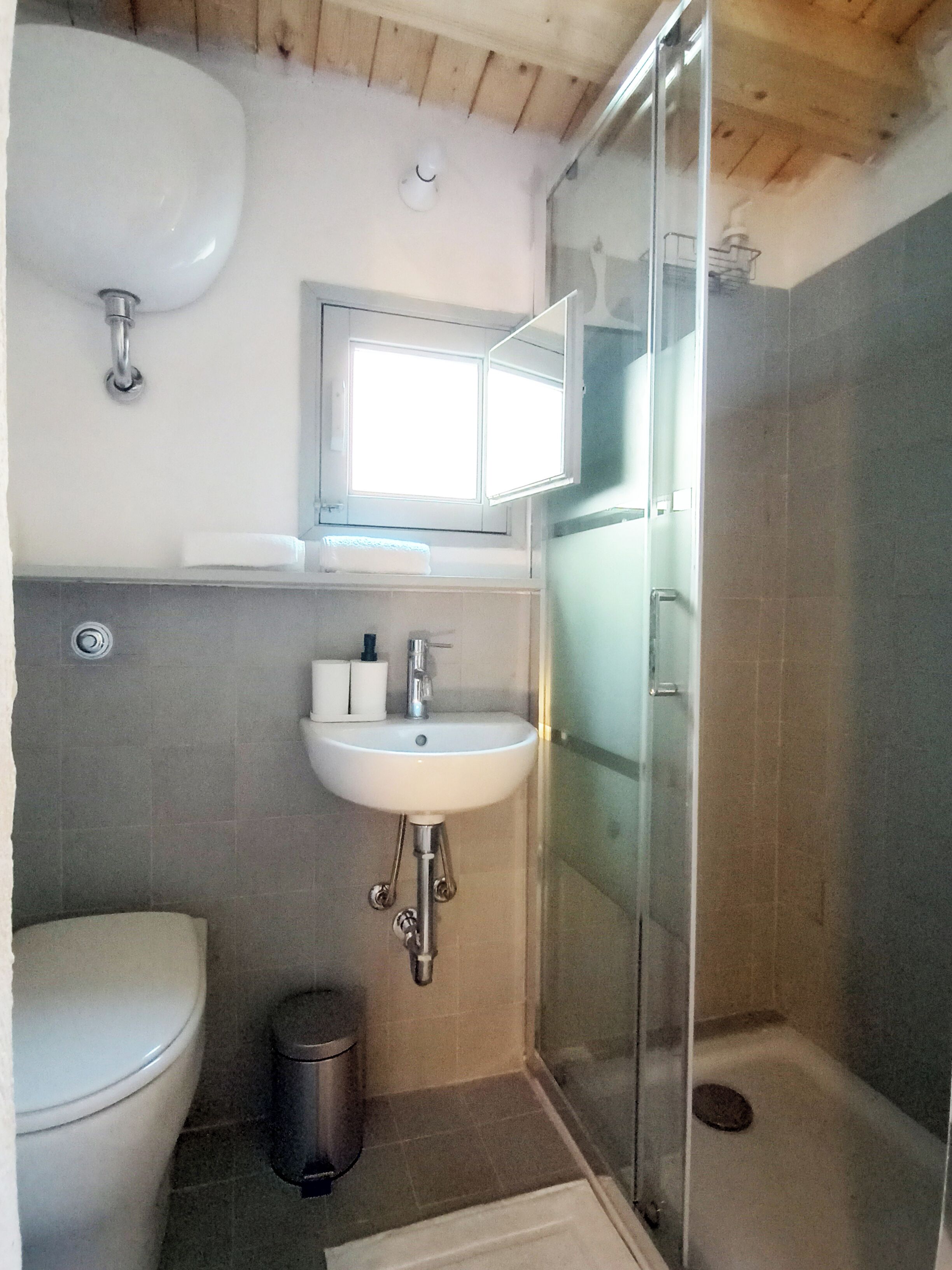 Un baño con inodoro, lavamanos y cabina de ducha con mampara de vidrio.
