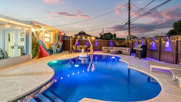 A backyard with a swimming pool, a covered seating area, and a barbecue grill.
