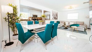 A modern living room with a sofa, a dining table with chairs, and a kitchen in the background.