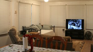 A living room with a sofa, a television, and a dining table with chairs. - Camp Gator #2 (Barataria)