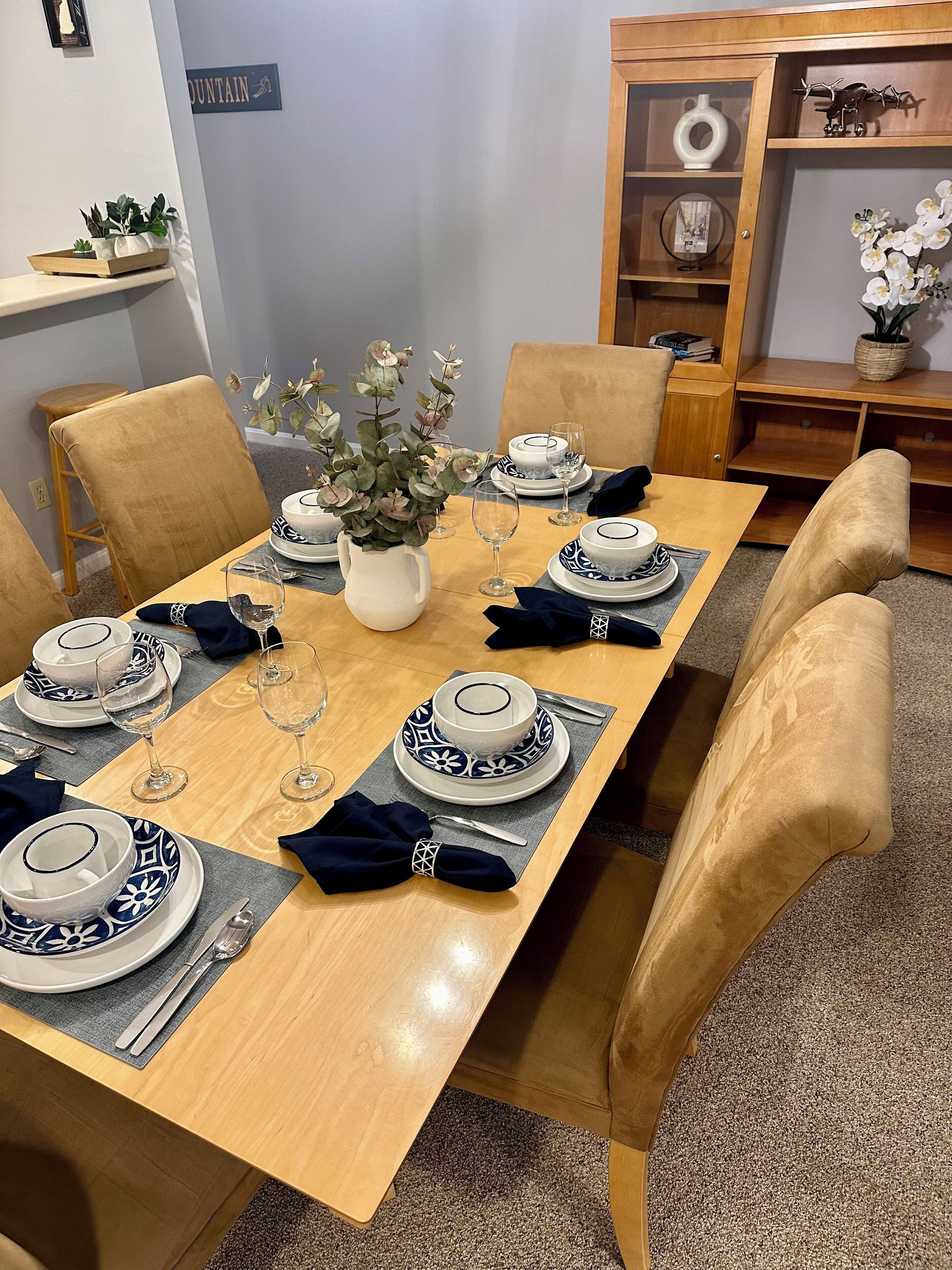 A dining table set with blue and white plates, glasses, and a vase of flowers.