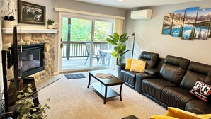 A living room with a stone fireplace, a television, a sofa, and a coffee table. - Loon Mountain Retreat at Lincoln NH (Lincoln)