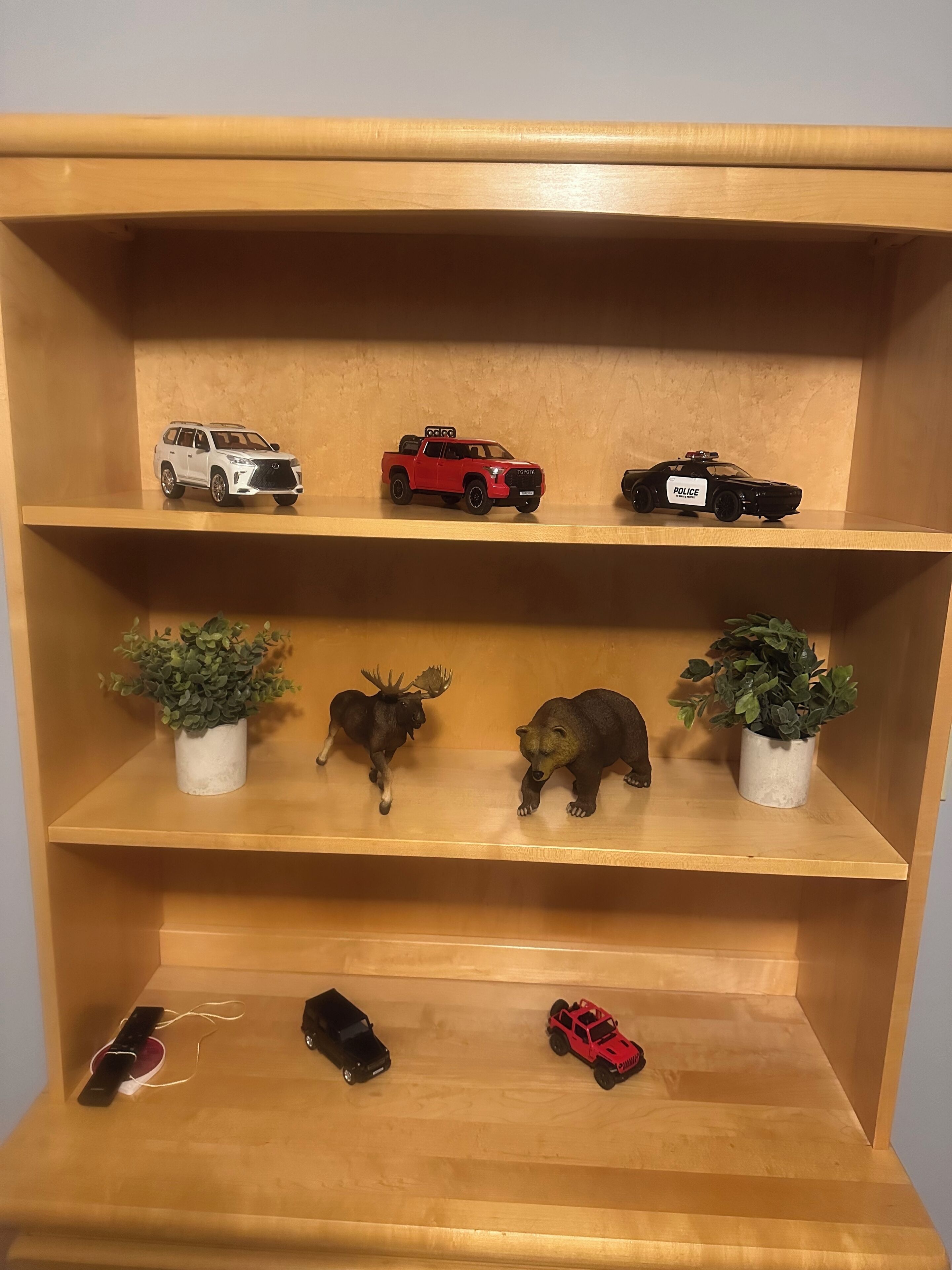 A wooden shelf with toy vehicles and animal figurines.