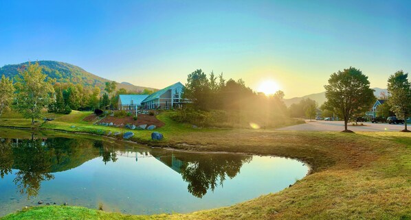 A serene landscape with a pond, a building with a blue roof, and a mountain in the background.