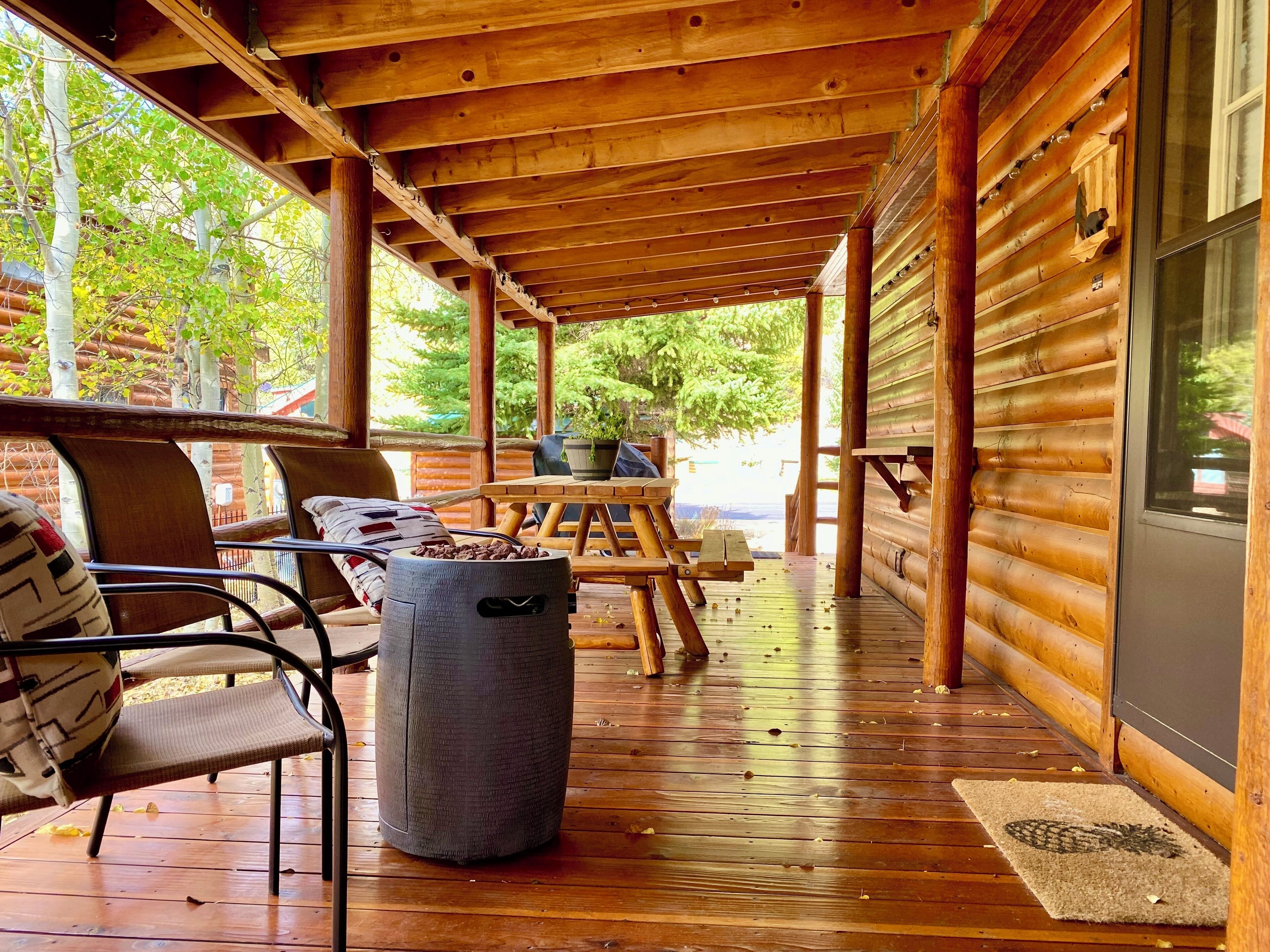 Eine Holzterrasse mit überdachter Sitzgruppe, einem Mülleimer und Blick ins Freie.