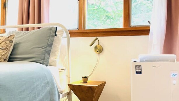 Una camera da letto con un letto, un comodino con una lampada, un termosifone e una finestra con tende.