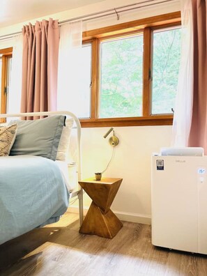 A bedroom with a bed, a bedside table with a lamp, a heater, and a window with curtains. - Catskills The Bohemian Dream (Shandaken)