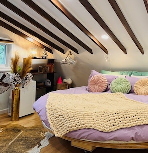 A bedroom with a bed, a bedside table, a lamp, a fan, and a window.