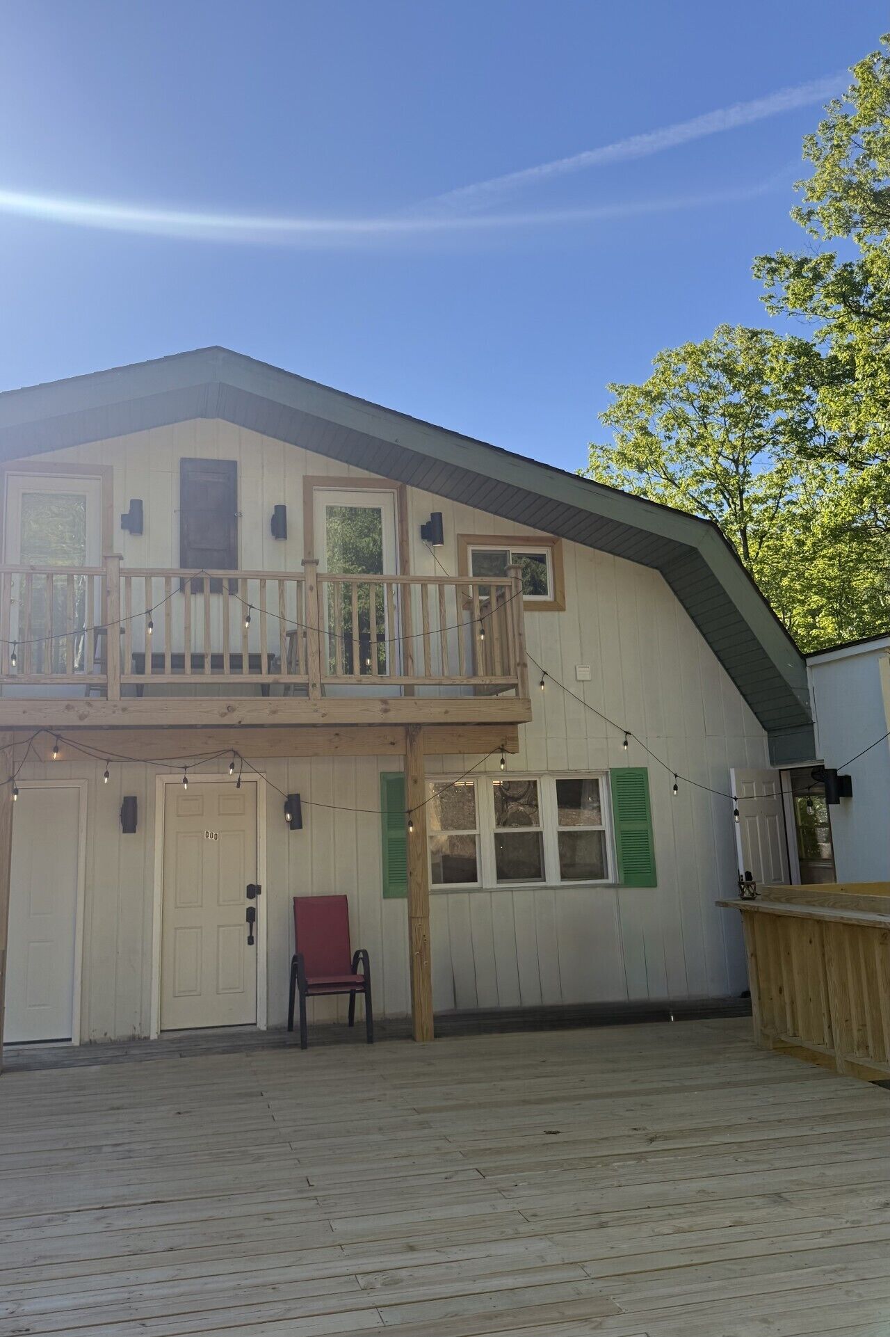 Een gebouw met twee verdiepingen, een balkon, een houten terras en een omheind gebied.