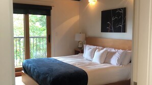 A bedroom with a wooden ceiling, a bed with white bedding, a nightstand with a lamp, and a window with a view of greenery. - Mariner's Loft Salt Spring Island - 2BDRM - Unit 201 (Salt Spring Island)