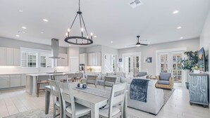 A spacious kitchen with white cabinets, a dining area with a table and chairs, and a living area with a sofa and a TV. - Favor 255 BE (Port Aransas)