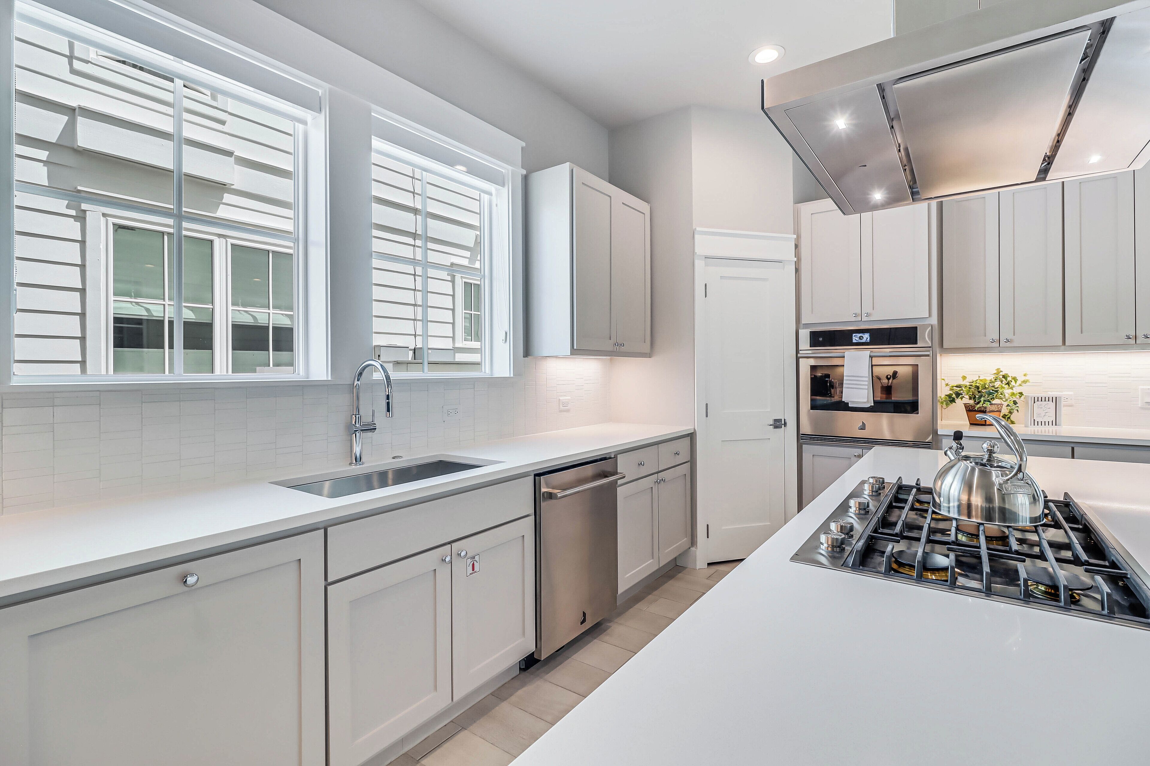 A modern kitchen with white cabinetry, a stainless steel dishwasher, a gas stove, and a built-in oven.