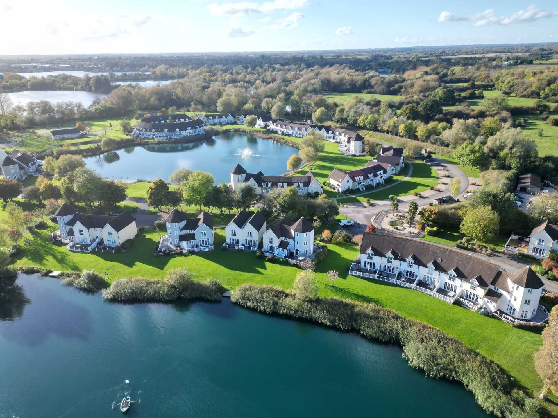 A lakeside residential area with white houses, a tower, and a boat on the water.