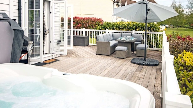 Une terrasse dotée d’un jacuzzi, de mobilier d’extérieur et d’un parasol.