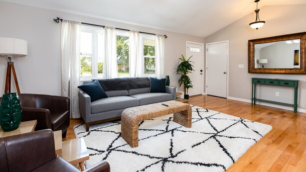 A living room with a grey sofa, a wooden coffee table, and a large mirror above a green console table. - TDJ Getaway<>4BR Home w/game room (South Bend)