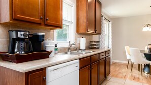 A kitchen with wooden cabinets, a dishwasher, a coffee maker, and a dining area with a table and chairs. - TDJ Getaway<>4BR Home w/game room (South Bend)