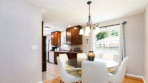 A dining area with a round table and white chairs, a chandelier, and a window with curtains. - TDJ Getaway<>4BR Home w/game room (South Bend)