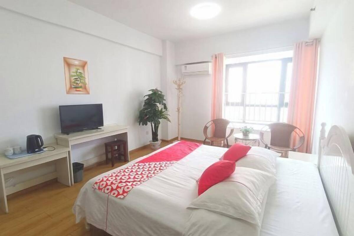Ein Hotelzimmer mit einem Bett, einem Schreibtisch mit Fernseher, einem Sessel, einem kleinen Tisch und einem Fenster mit Vorhängen.