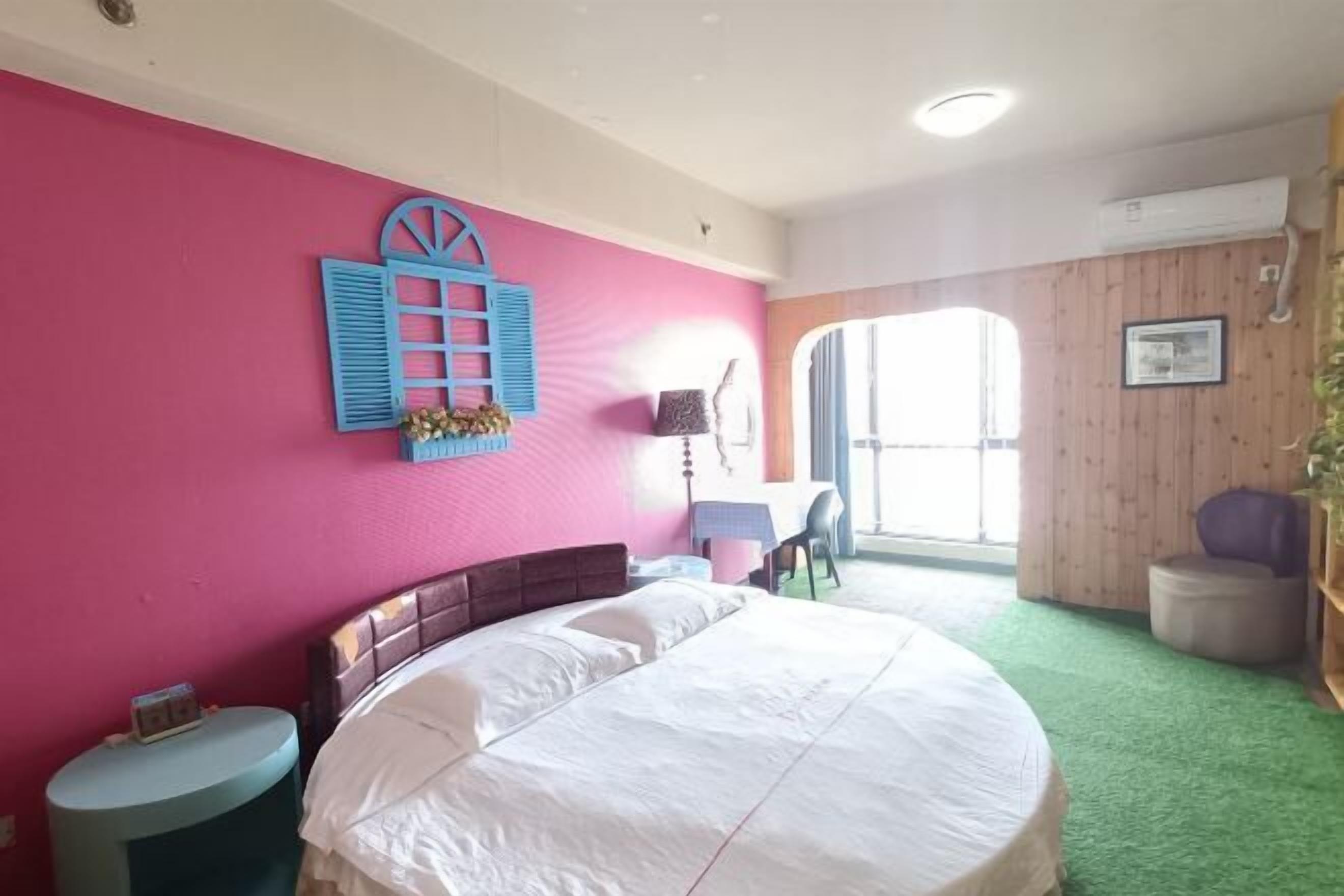 A bedroom with a large bed, a small table, a chair, and a window with a view.