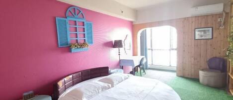 A bedroom with a large bed, a small table, a chair, and a window with a view.