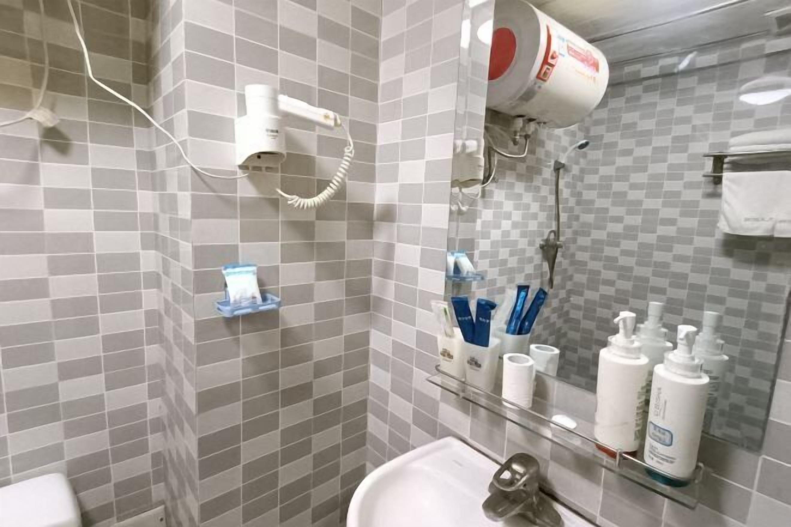 A bathroom with a white sink, a mirror, a hairdryer, and toiletries on a shelf.