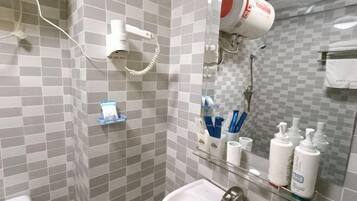A bathroom with a white sink, a mirror, a hairdryer, and toiletries on a shelf.