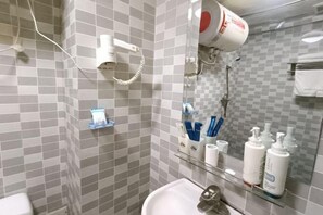 Ein Badezimmer mit einem weißen Waschbecken, einem Spiegel, einem Föhn und Pflegeprodukten auf einem Regal.