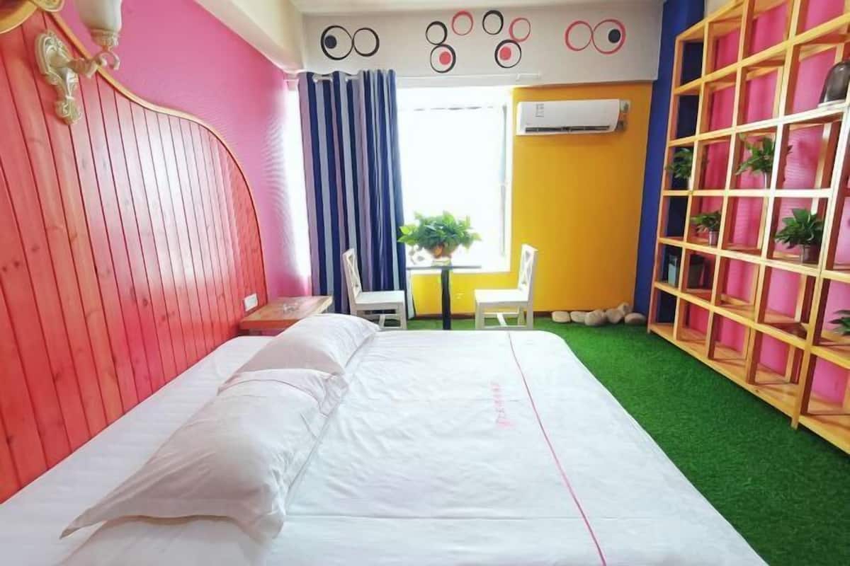 Ein Zimmer mit einem Bett, einem Sessel, einem kleinen Tisch mit einer Pflanze und einem Fenster mit Vorhängen.