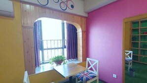 Une pièce avec une table en bois, deux chaises ornées de coussins à motifs Union Jack, une plante en pot et une fenêtre avec des rideaux.
