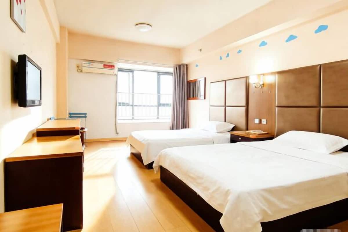 Ein Hotelzimmer mit zwei Betten, einem Fernseher, einem Schreibtisch und einem Fenster mit Vorhängen.