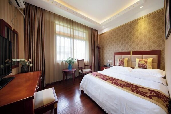 Una habitación de hotel con una cama grande, un escritorio, una silla y una mesita con un florero.