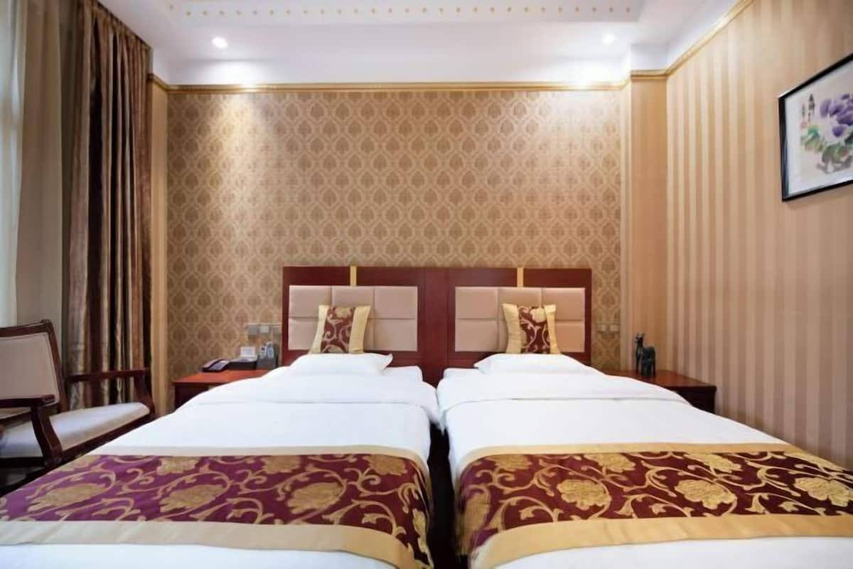 A hotel room with two beds, a wooden headboard, a nightstand with a phone, and a chair.